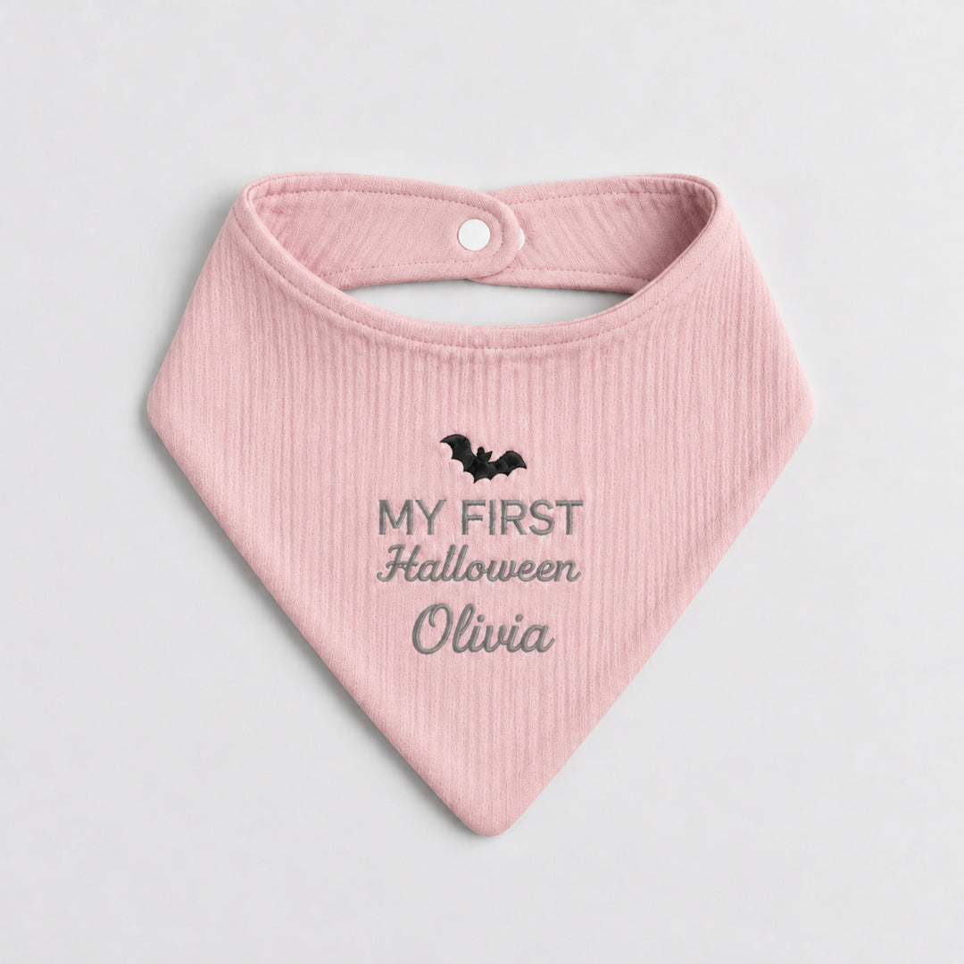 Personalised pastel pink baby bandana bib featuring a black embroidered bat, grey “My First Halloween” lettering and the name Olivia.