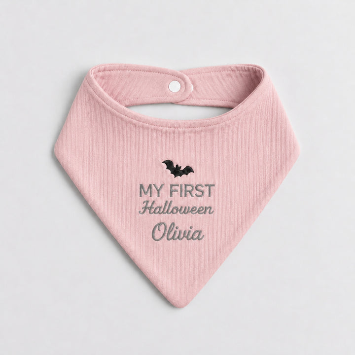 Personalised pastel pink baby bandana bib featuring a black embroidered bat, grey “My First Halloween” lettering and the name Olivia.