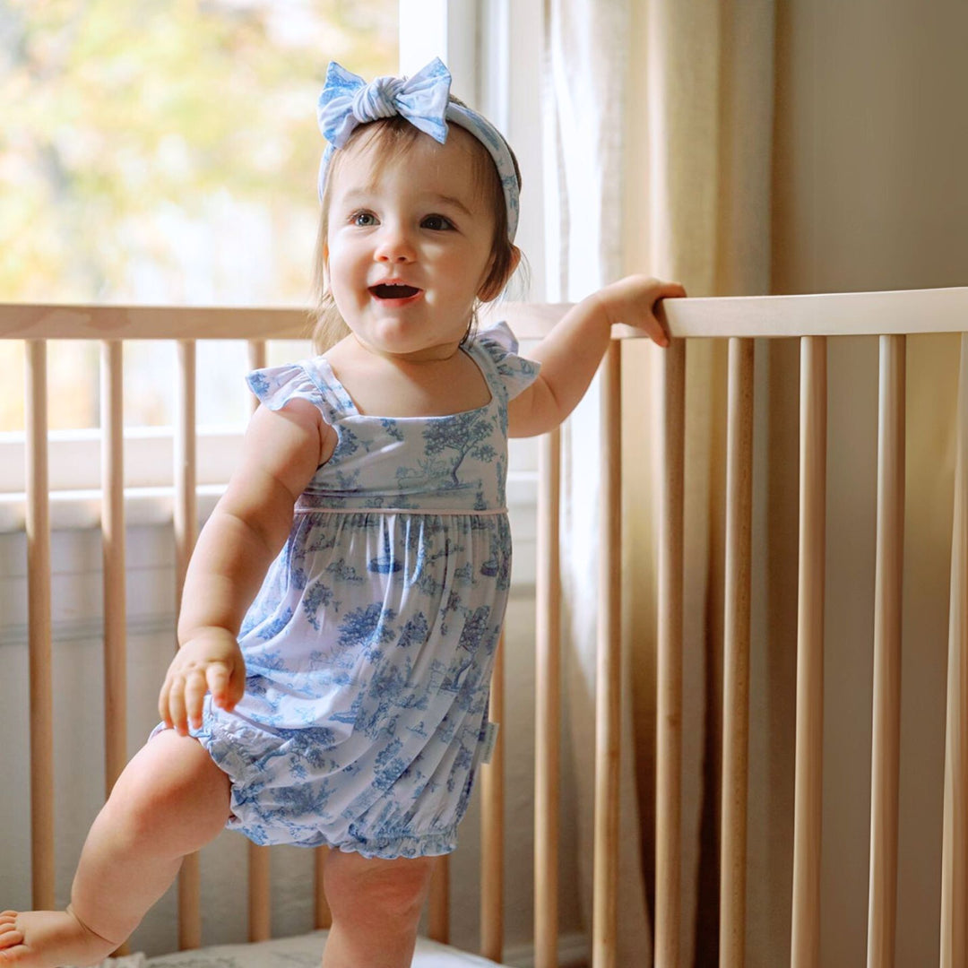 Baby wearing House of Holly Garden Toile Ruffle Bubble Romper in Blue
