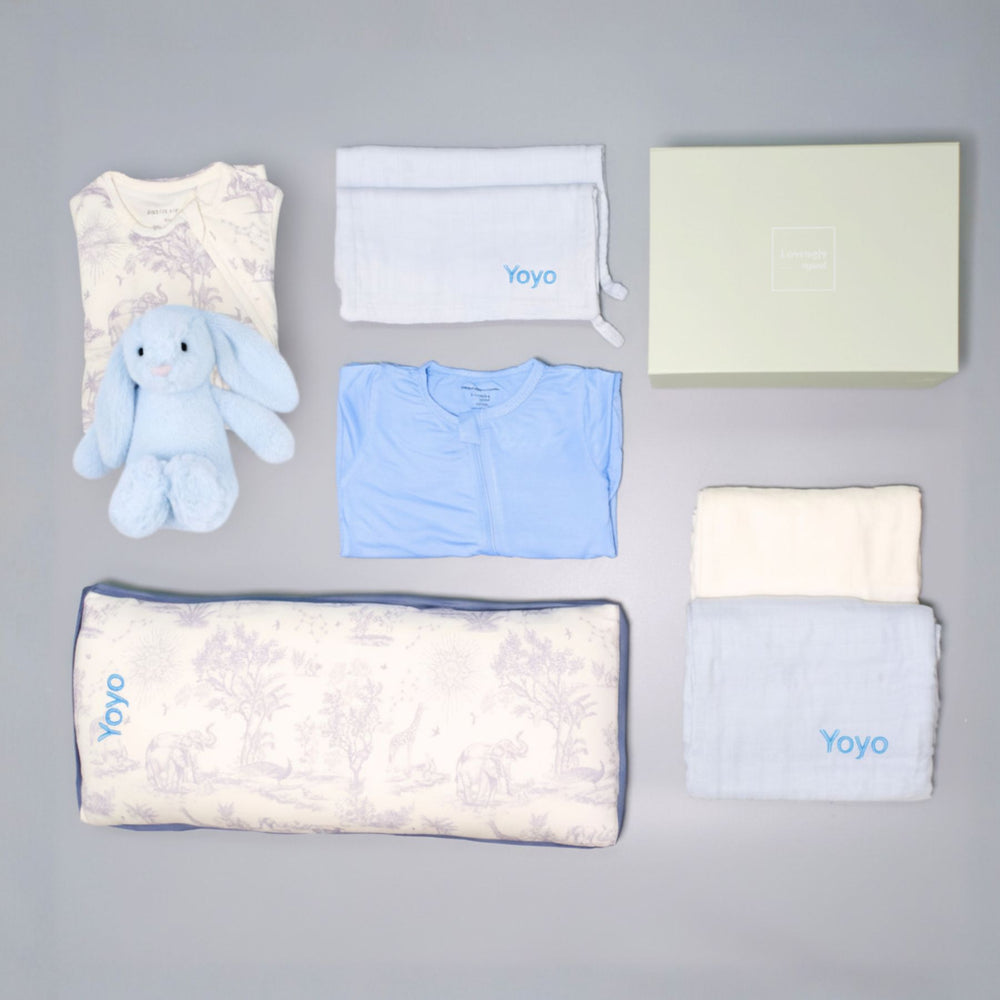 Collection of baby items including a blue plush toy, baby clothes, and blankets on a gray background.