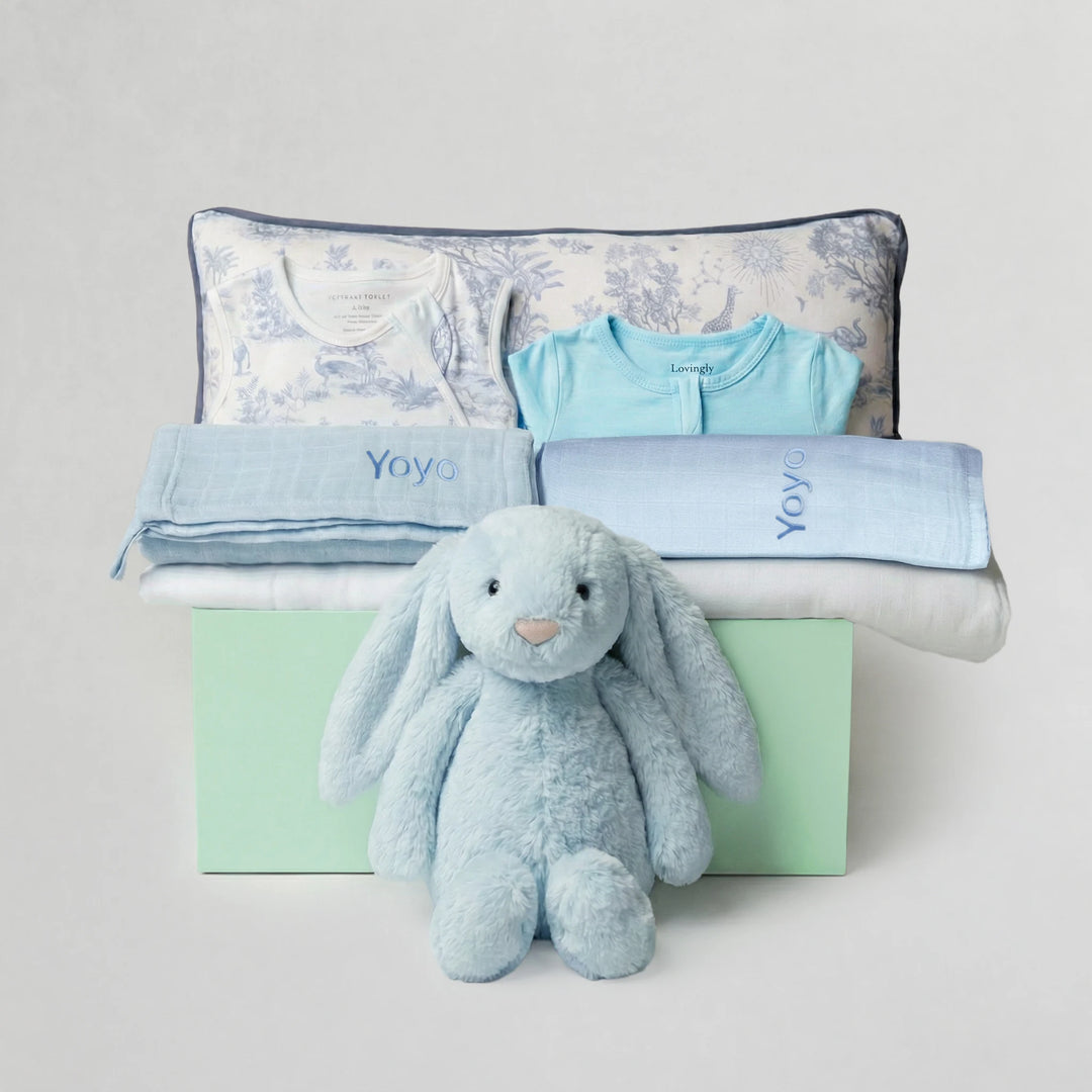Collection of baby items including a blue plush toy, baby clothes, and blankets on a gray background.