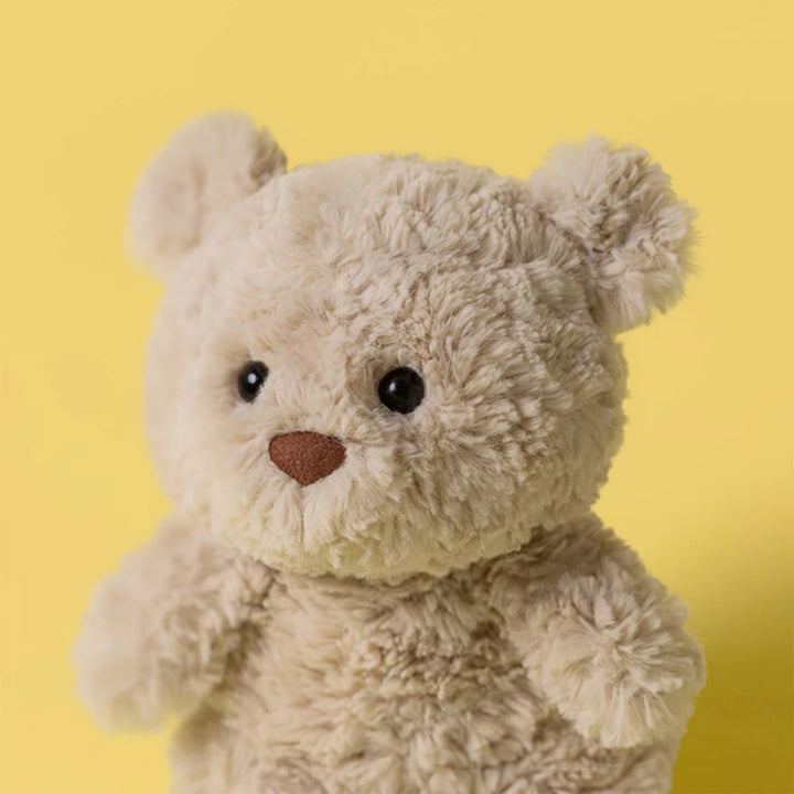 Close-up of Bartholomew Bear Junior showing its soft cream fur, round ears, black eyes and brown nose against a yellow background.