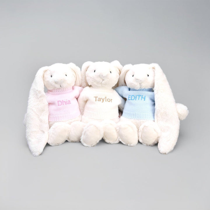 Three stuffed bunnies in sweaters with names