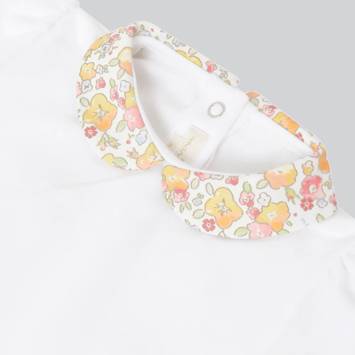 Close up of Marie Chantal's White baby onesie with floral ruffle collar