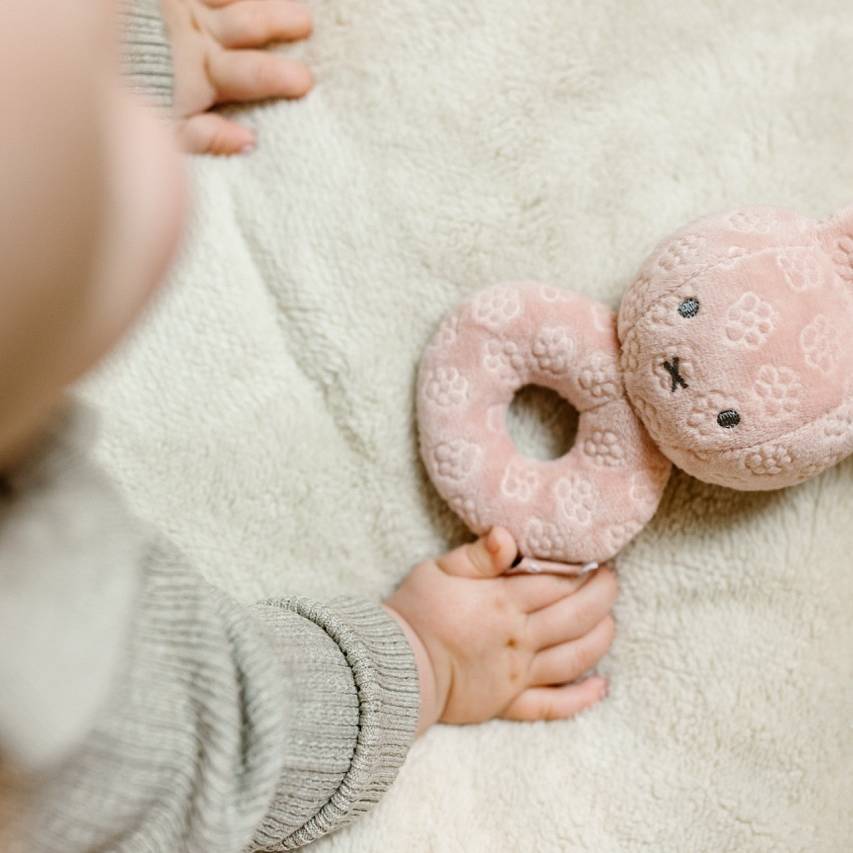 Child holding a pink miffy flower rattle toy on a soft surface