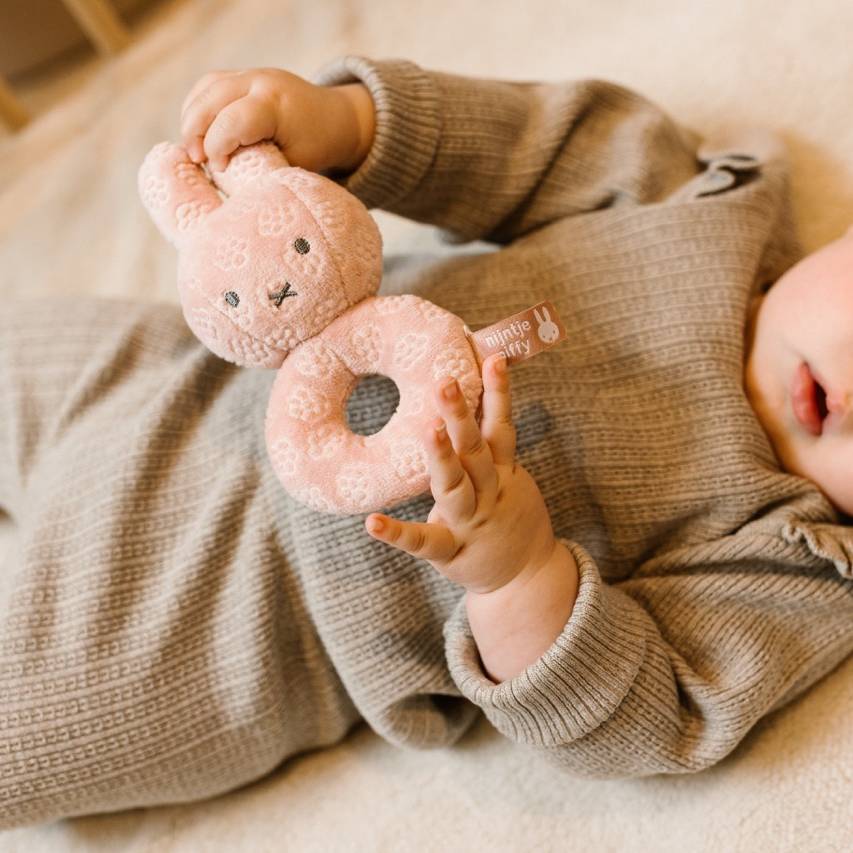 Baby holding a pink miffy flower rattle toy with a soft focus background