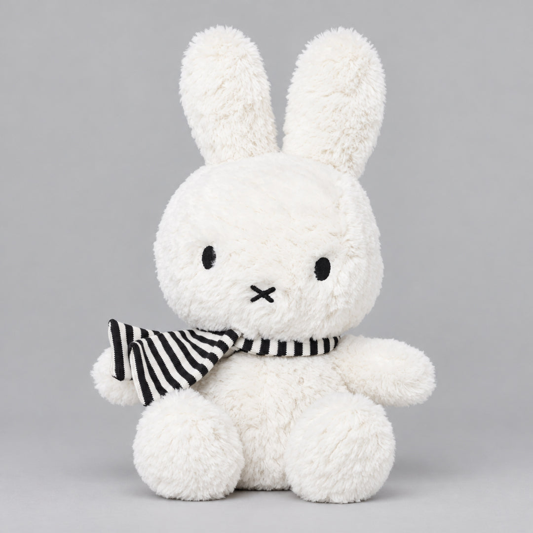 White Miffy bunny soft toy sitting with a black and white striped scarf, featuring long upright ears and soft fluffy fur.
