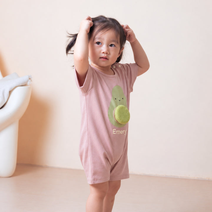Toddler wearing the personalised dusty pink avocado romper with the name “Emery,” standing in a bright neutral room.