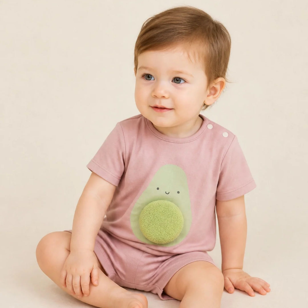 Baby wearing a dusty pink avocado romper with a 3D textured avocado detail, sitting against a soft neutral background.