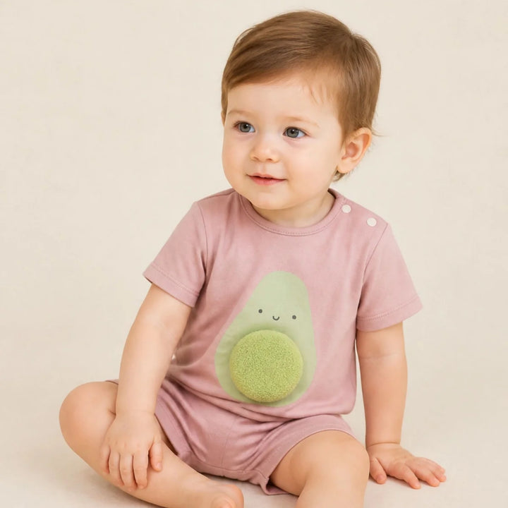 Baby wearing a dusty pink avocado romper with a 3D textured avocado detail, sitting against a soft neutral background.