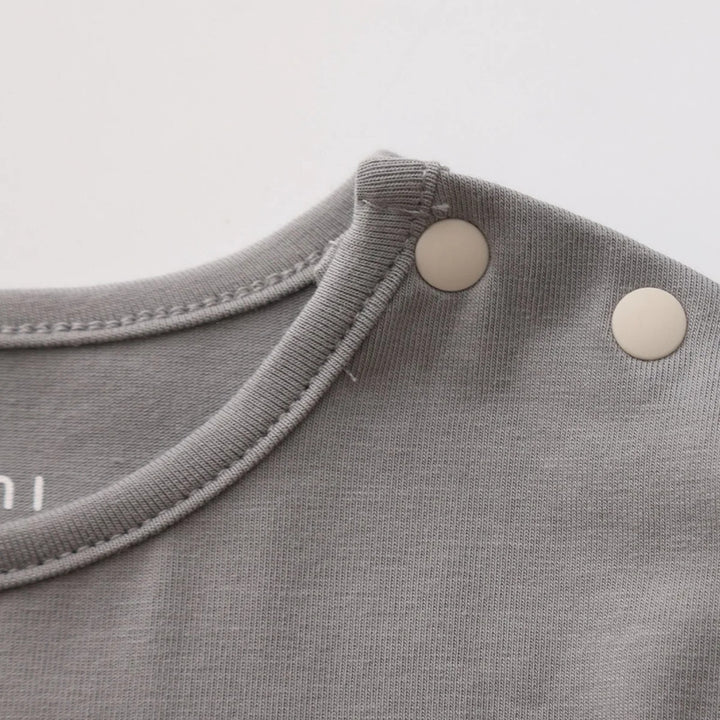 Close-up of a grey baby romper showing the soft fabric, neckline stitching and two cream snap buttons at the shoulder.