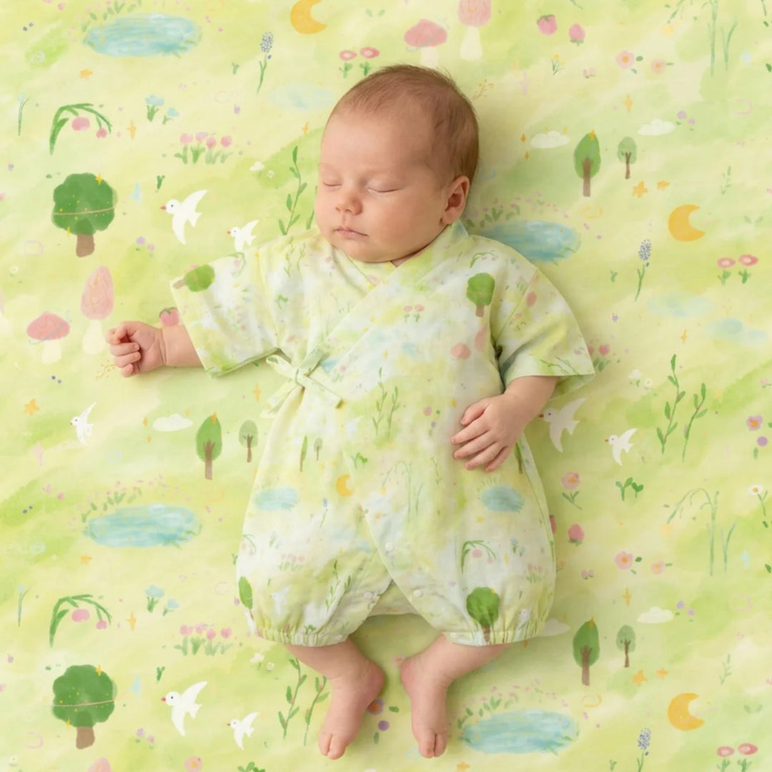 Sleeping baby wearing a light green garden-print kimono romper on matching illustrated bedding.