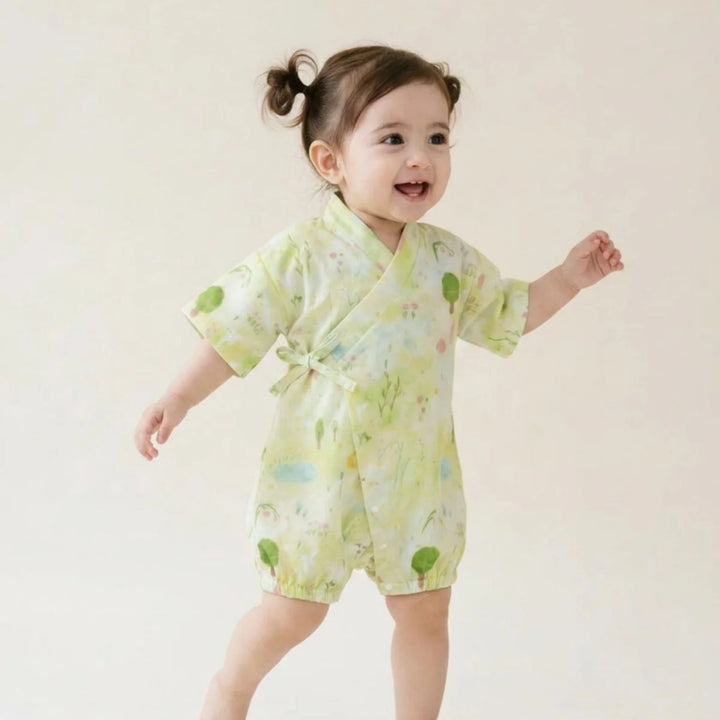 Smiling toddler wearing a light green garden-print kimono romper with short sleeves and wrap-front tie detail.