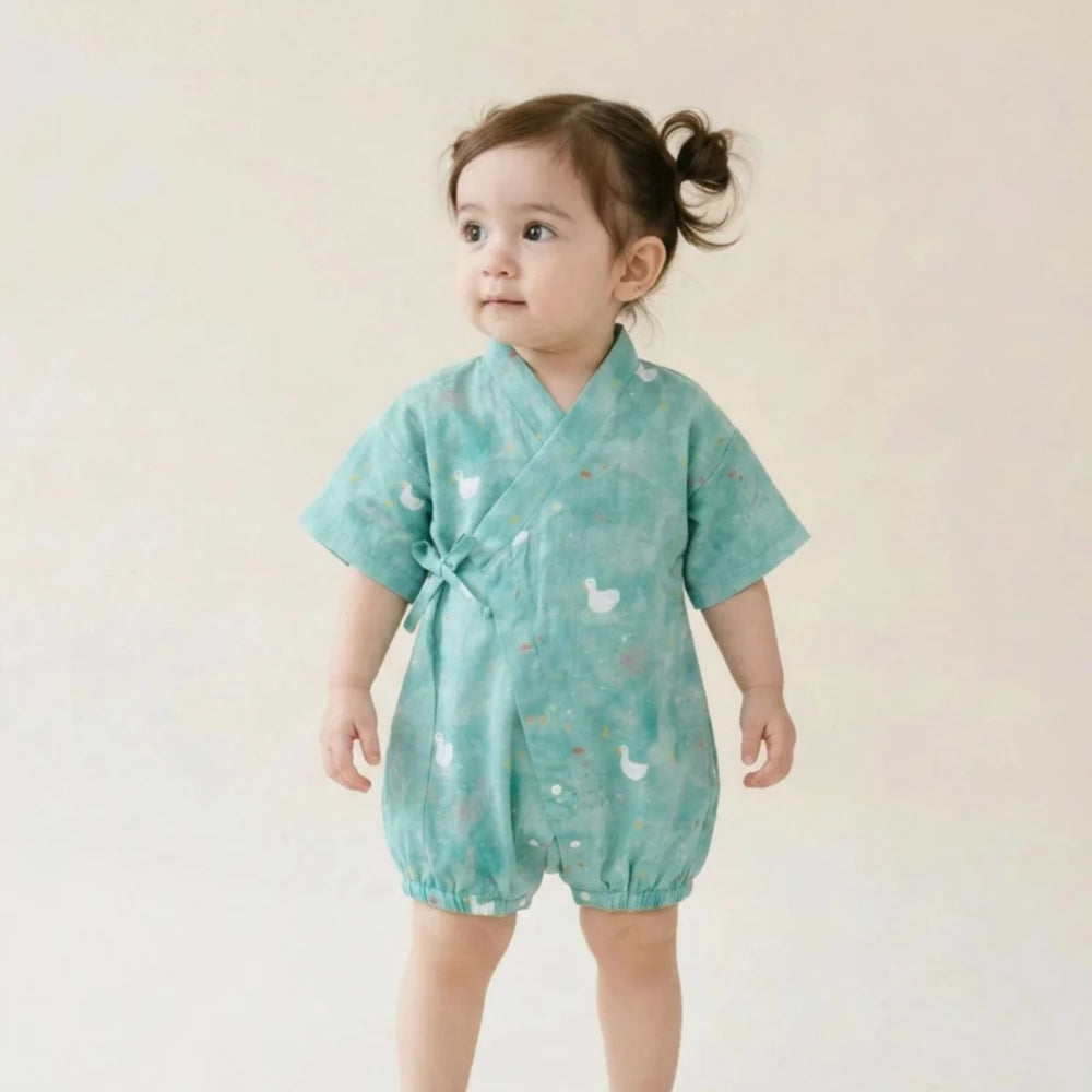 Toddler wearing a teal duck-print kimono romper with wrap-front tie detail against a soft neutral background.