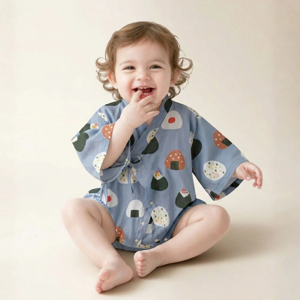 Smiling baby wearing a light blue onigiri-print kimono romper while sitting against a soft neutral background.