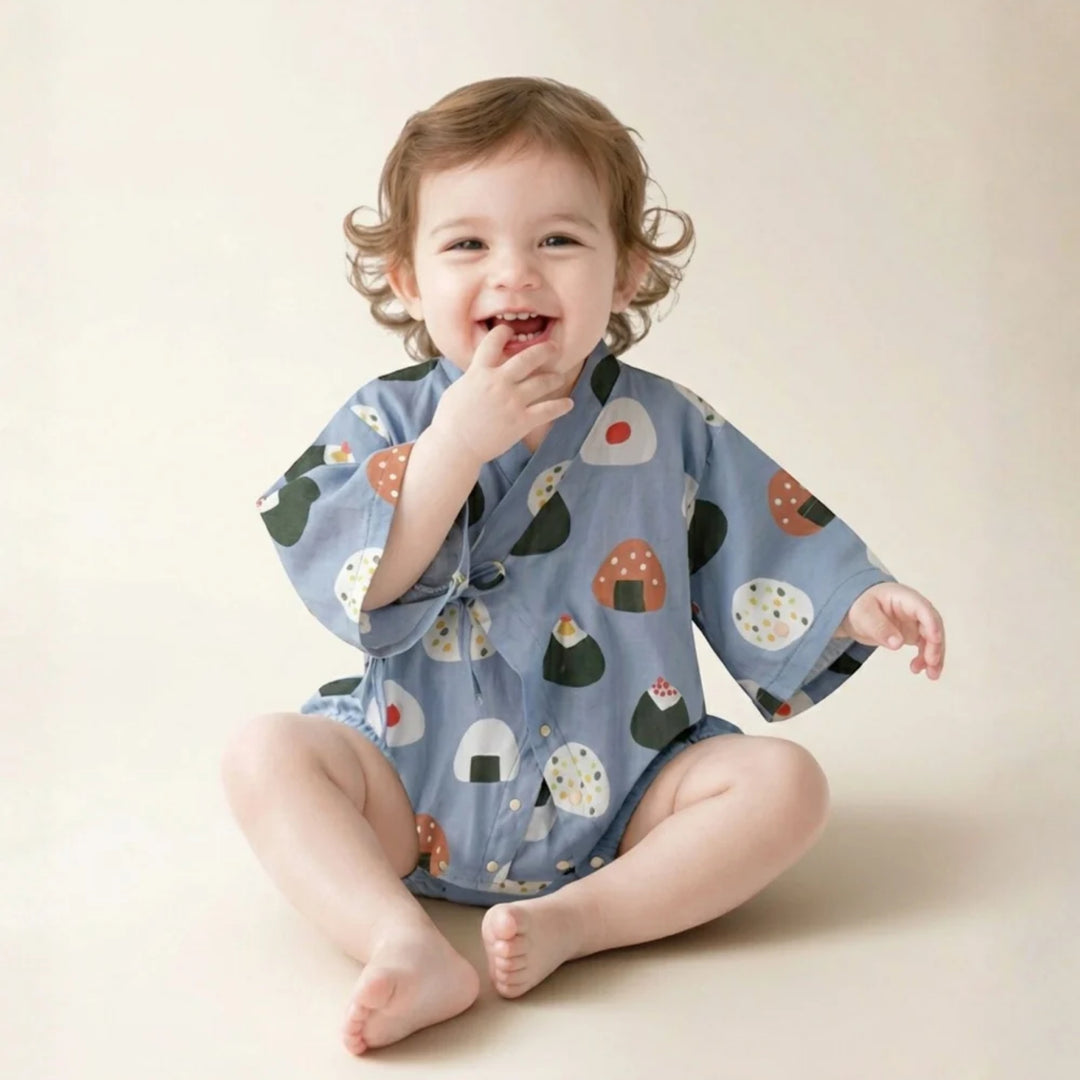 Smiling baby wearing a light blue onigiri-print kimono romper while sitting against a soft neutral background.