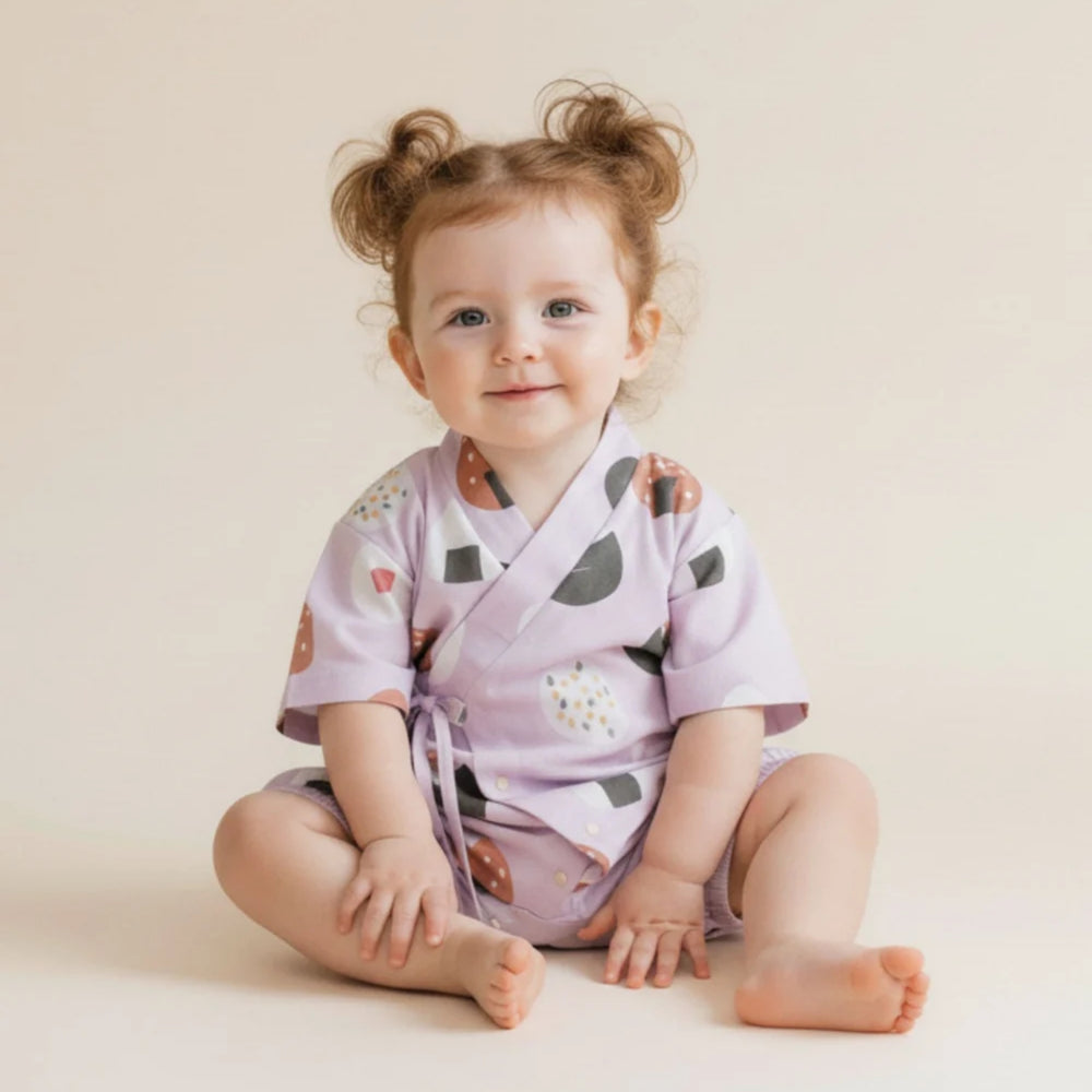 Baby girl wearing a lilac onigiri-print kimono romper, sitting against a soft neutral background.