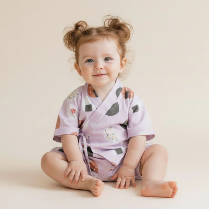 Baby girl wearing a lilac onigiri-print kimono romper, sitting against a soft neutral background.