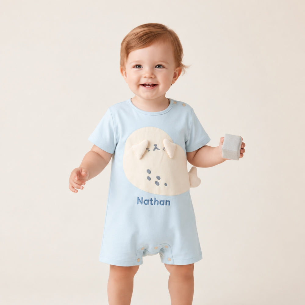 Smiling baby wearing a light blue personalised seal romper with the name “Nathan,” featuring a cream seal applique and 3D flippers.