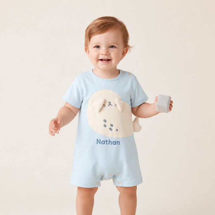 Smiling baby wearing a light blue personalised seal romper with the name “Nathan,” featuring a cream seal applique and 3D flippers.