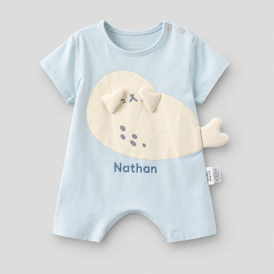 Light blue short-sleeve baby romper with a cream seal applique, 3D flippers and tail detail, personalised with the name “Nathan.”