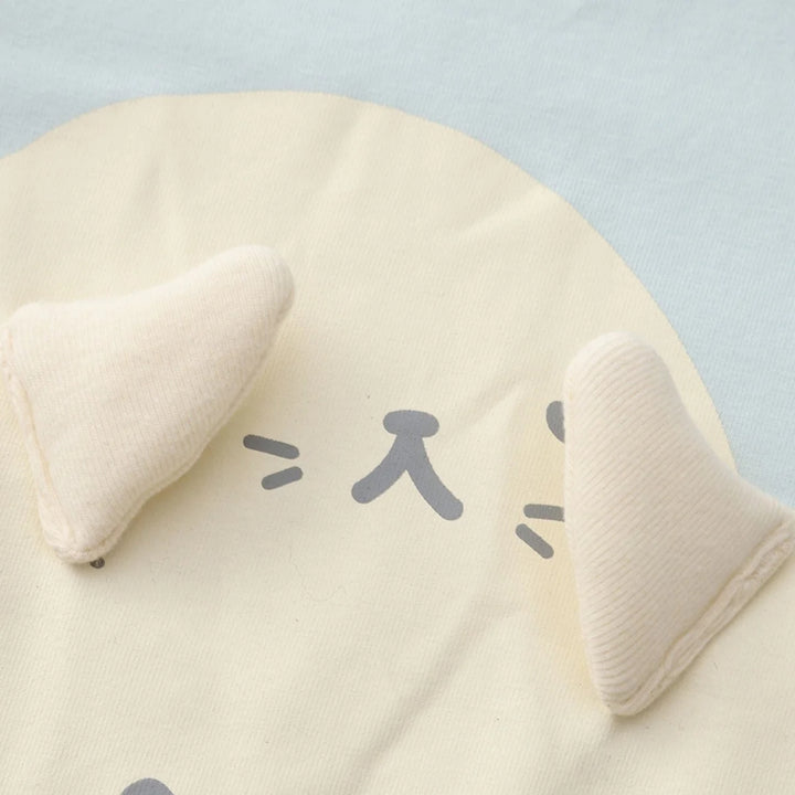 Close-up of a light blue baby romper showing the cream seal applique with soft 3D flippers and grey facial details.