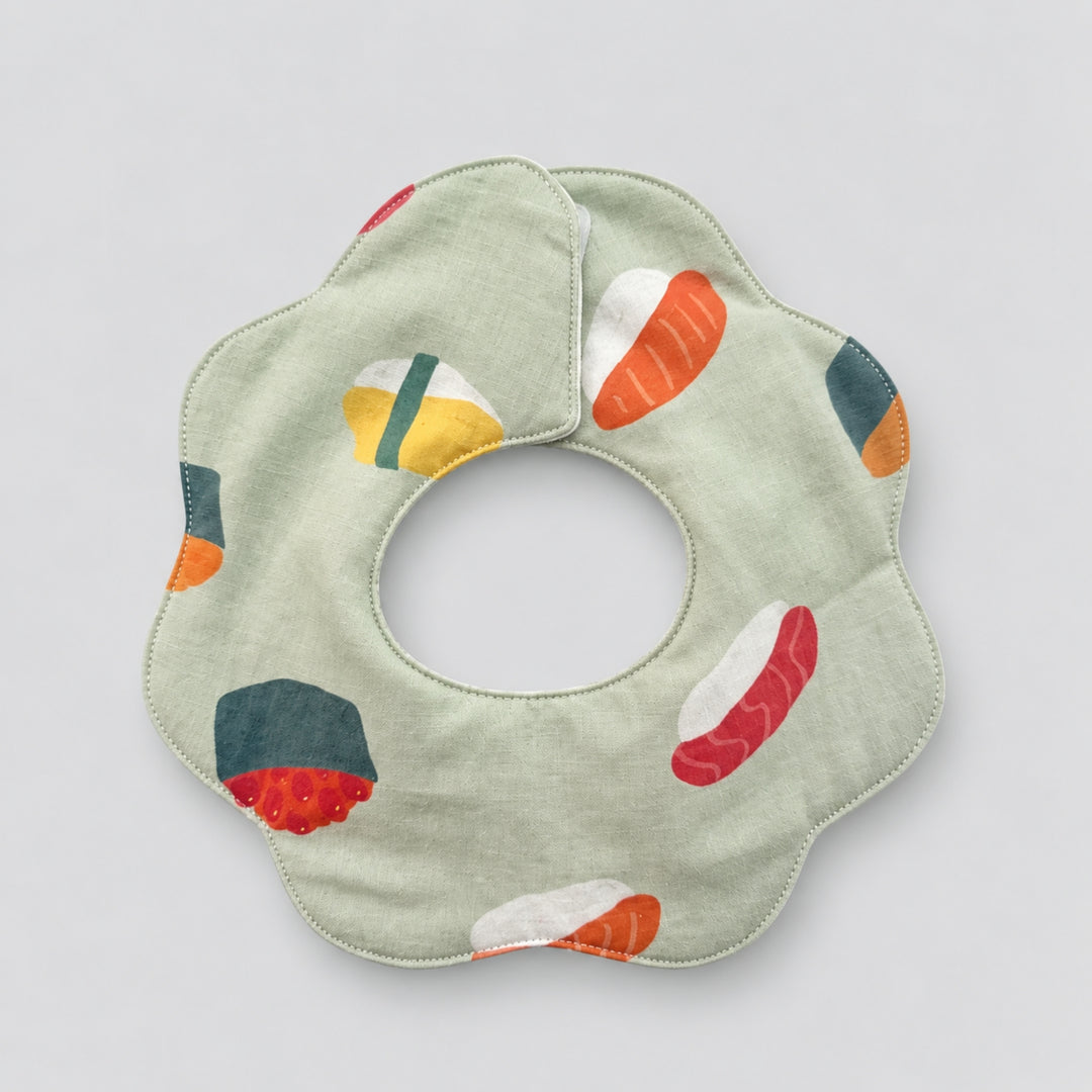 Back view of a soft green scalloped baby bib featuring colourful sushi illustrations and a rounded neck opening.