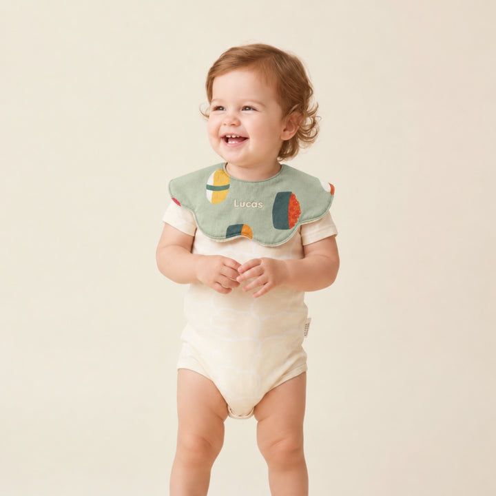 Smiling baby wearing a green sushi-print bib personalised with the name “Lucas,” paired with a cream bodysuit.