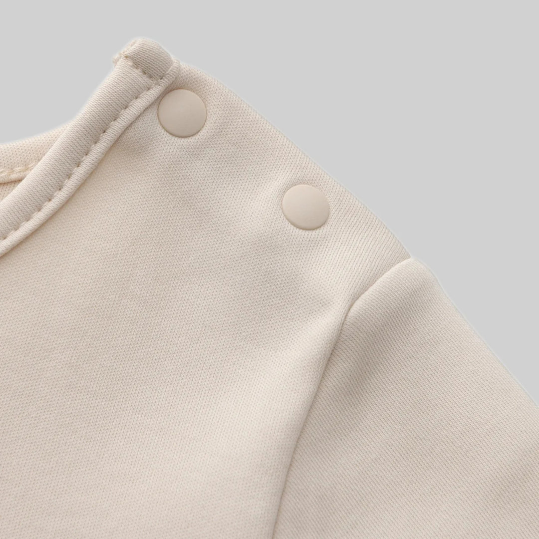 Close-up of the cream tempura romper showing the soft fabric, neckline stitching and two cream snap buttons at the shoulder.