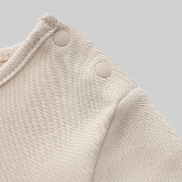 Close-up of the cream tempura romper showing the soft fabric, neckline stitching and two cream snap buttons at the shoulder.