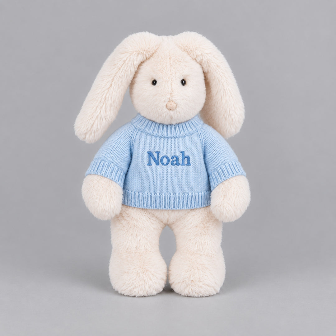 Personalised cream bunny soft toy wearing a blue knitted jumper embroidered with the name Noah.