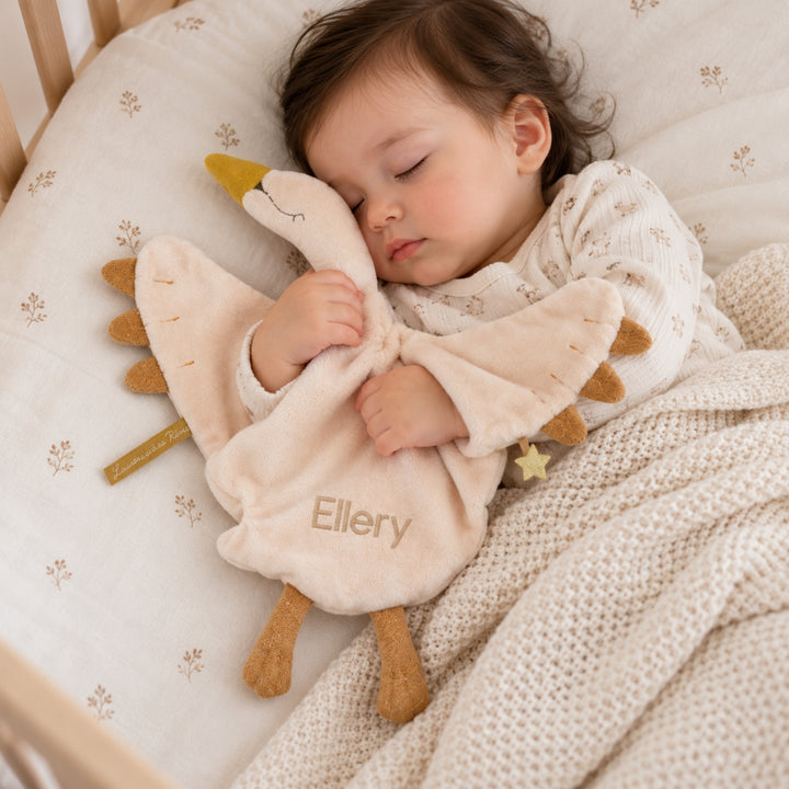 Sleeping baby cuddling a cream Moulin Roty swan comforter, personalised with the name Ellery in beige embroidery, featuring golden wings and soft plush fabric.