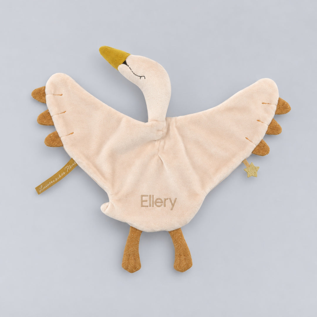 Cream Moulin Roty swan comforter with outstretched wings, mustard-gold beak and feet, and the name Ellery embroidered in beige thread.