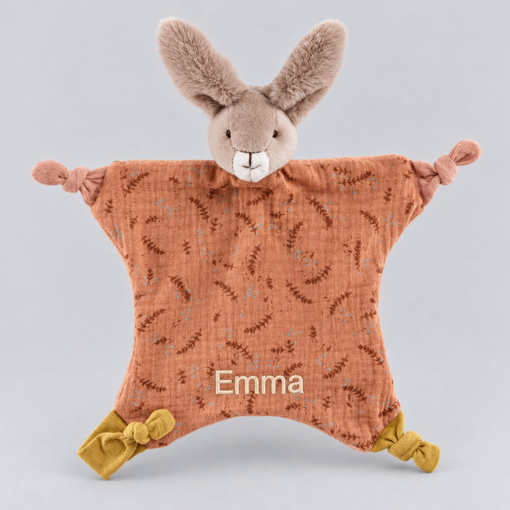 Moulin Roty rabbit comforter featuring a soft taupe bunny head, terracotta floral-patterned fabric, knotted corners and the name Emma embroidered in cream thread.