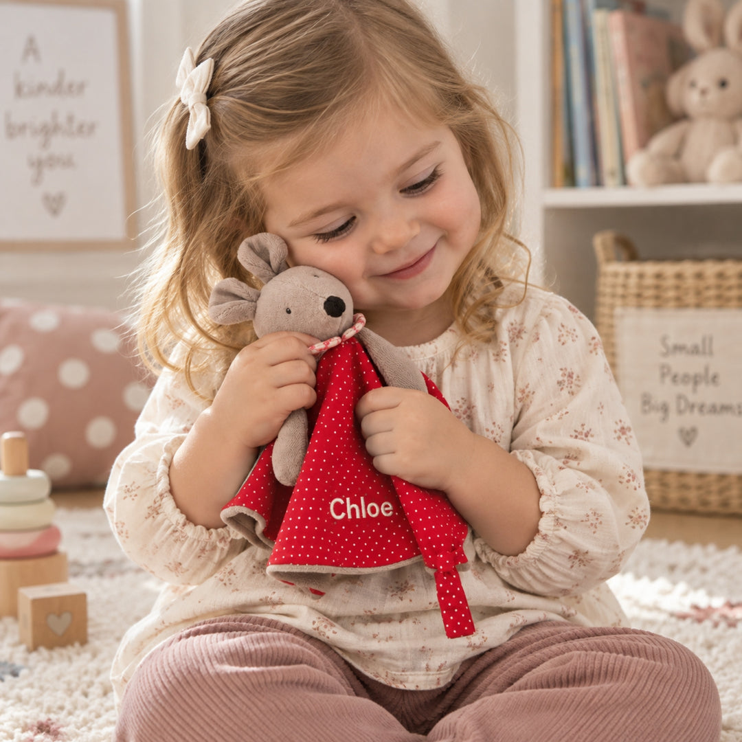 Little girl cuddling a personalised Moulin Roty Nini the Mouse comforter embroidered with the name “Chloe” in a cosy nursery setting.