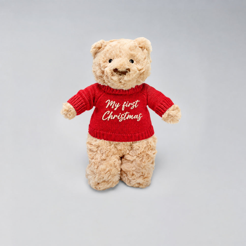 Personalised Christmas teddy bear wearing a red knitted jumper with “My First Christmas” embroidered in cream on the front, photographed against a light grey studio background.
