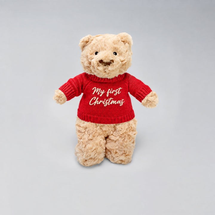 Personalised Christmas teddy bear wearing a red knitted jumper with “My First Christmas” embroidered in cream on the front, photographed against a light grey studio background.