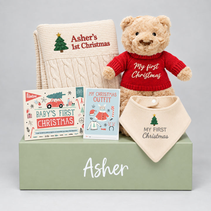 Personalised My First Christmas gift set featuring a cream cable knit blanket embroidered with a Christmas tree and “Asher’s 1st Christmas,” a teddy bear wearing a red “My First Christmas” jumper, a Baby’s First Christmas milestone book, a Christmas outfit booklet, and a cream “My First Christmas” bib, arranged on a sage green personalised gift box with the name “Asher.”