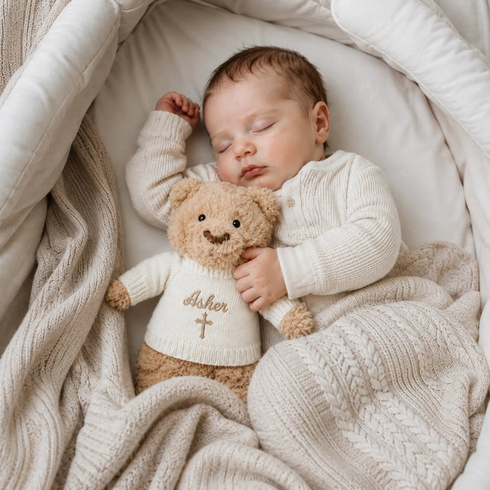 Sleeping newborn baby cuddling personalised Christian teddy bear with embroidered name Asher and cross