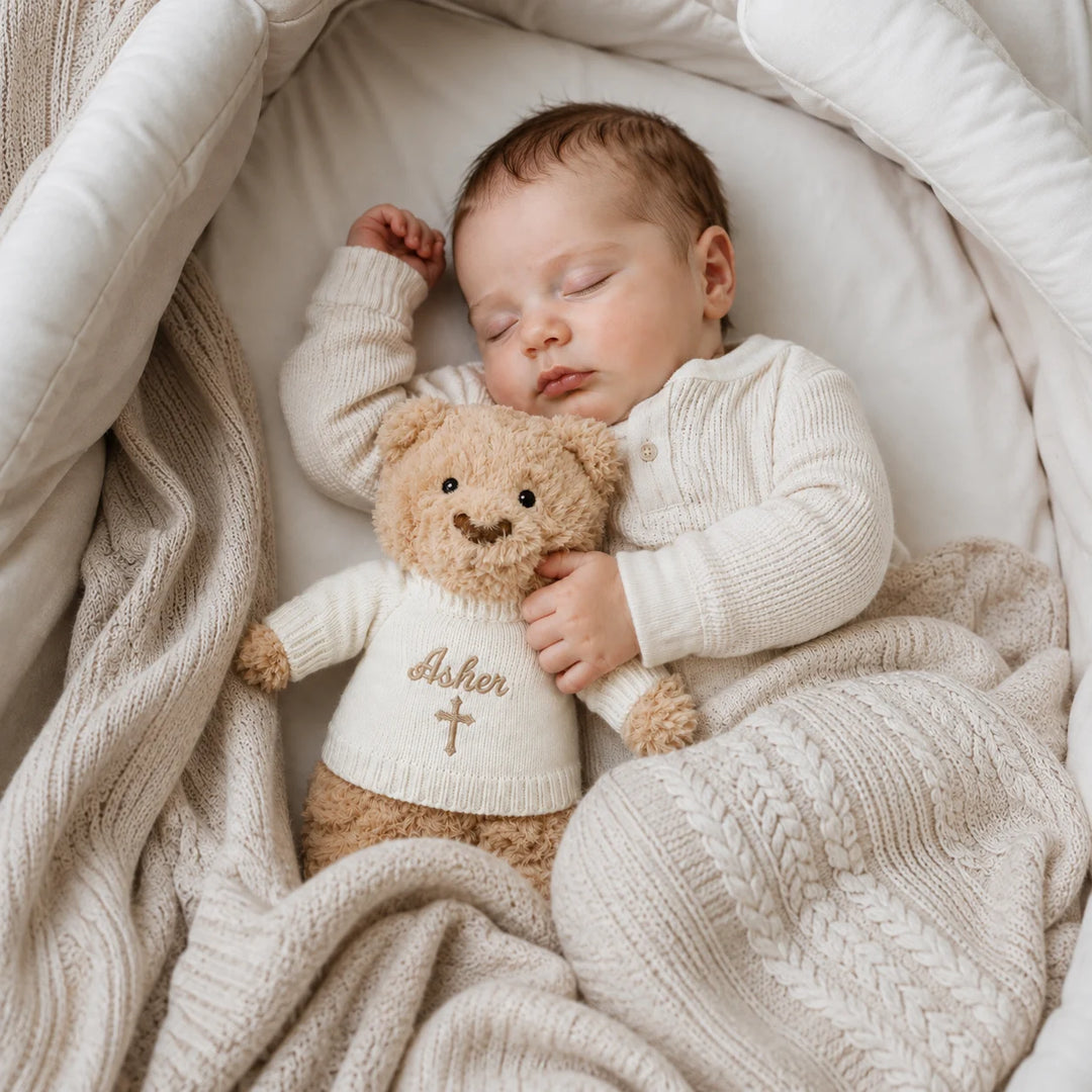 Sleeping newborn baby cuddling personalised Christian teddy bear with embroidered name Asher and cross