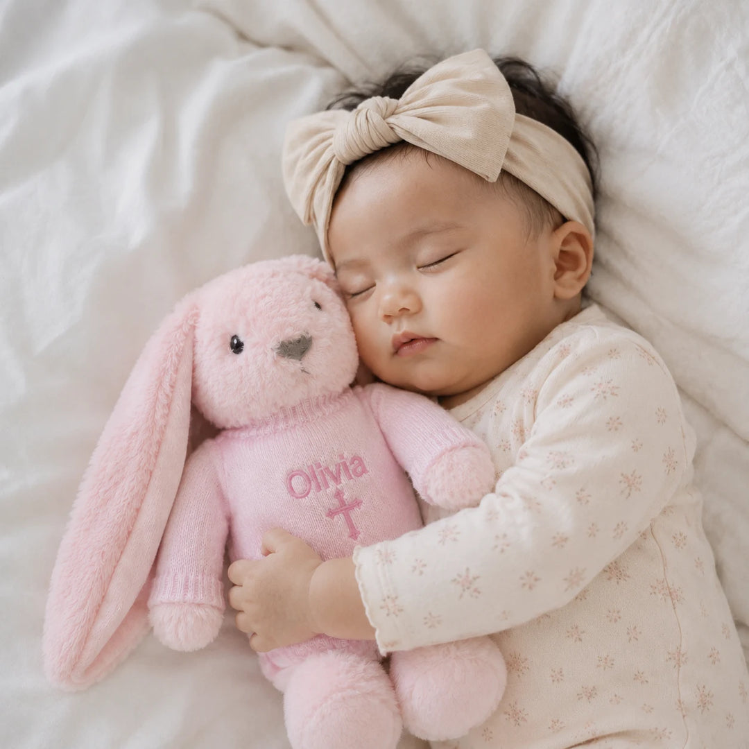 Sleeping baby girl cuddling personalised pink Christian bunny with embroidered name Olivia and cross
