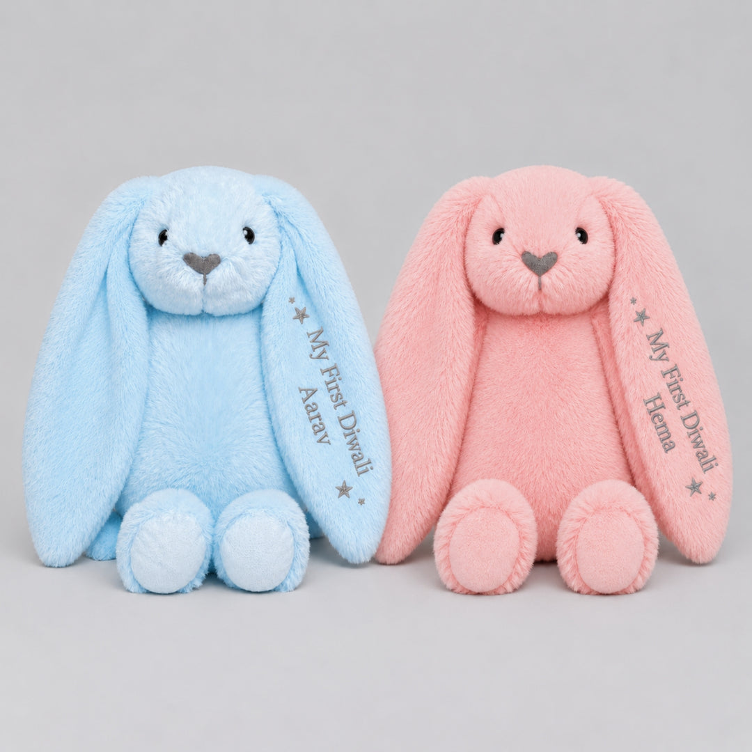Personalised blue and pink Diwali bunny soft toys sitting side by side, each embroidered on the ear with “My First Diwali” and the child’s name.