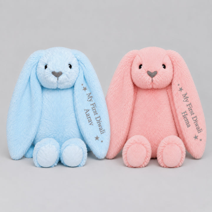Personalised blue and pink Diwali bunny soft toys sitting side by side, each embroidered on the ear with “My First Diwali” and the child’s name.