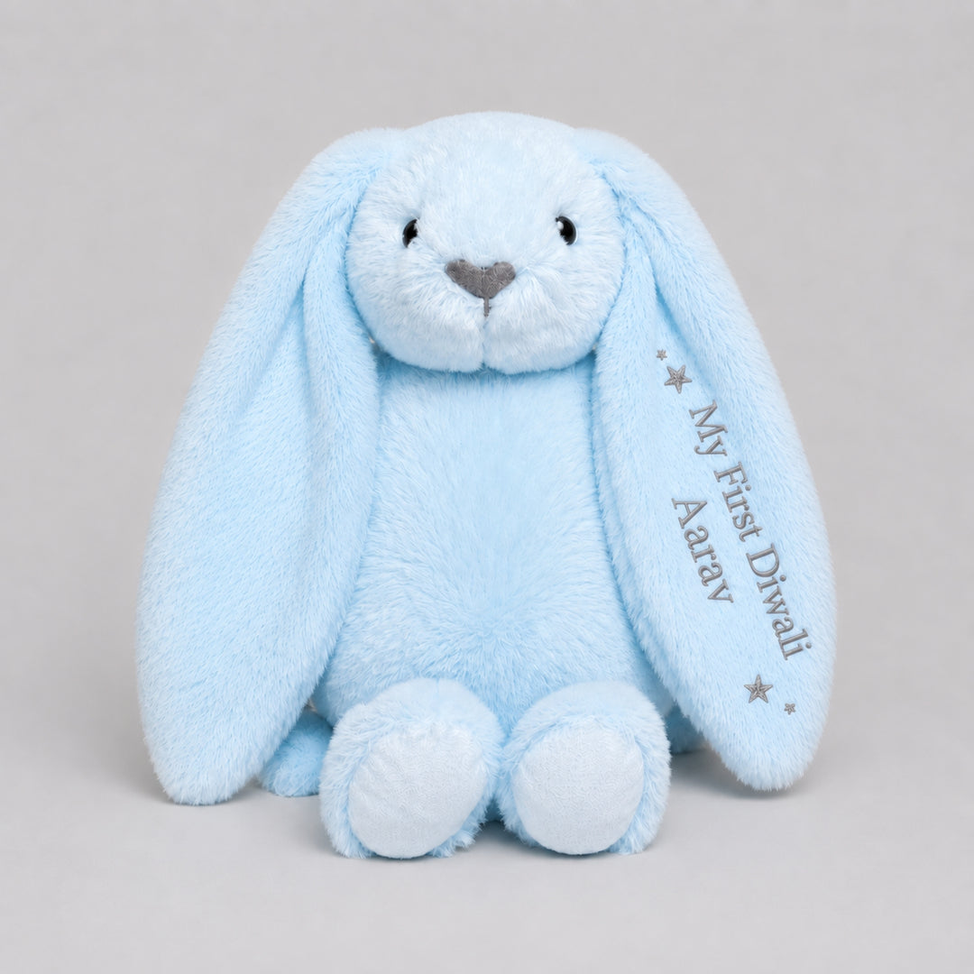 Personalised baby blue bunny soft toy embroidered with “My First Diwali Aarav” and star details on the ear, photographed on a light grey studio background.