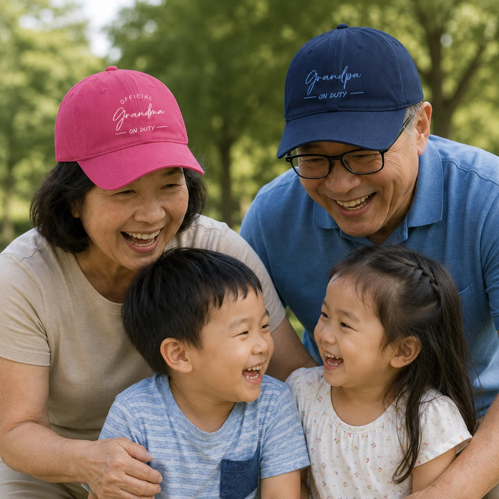 Asian grandma and grandpa wearing personalised “Official Grandma On Duty” and “Grandpa On Duty” caps, laughing with their grandchildren outdoors.