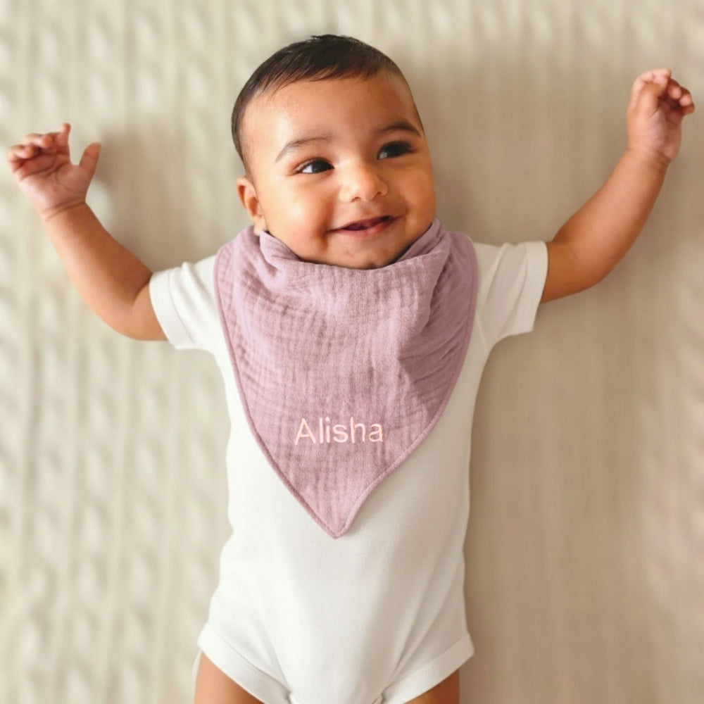 Baby wearing a white onesie with a pink bib labeled 'Alisha' on a neutral background