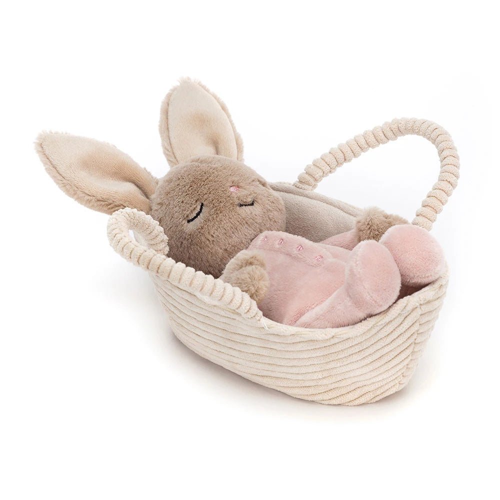 Jellycat Rock-a-Bye Bunny peacefully sleeping in a cordy beige basket, with praline fur and a sweet pink onesie