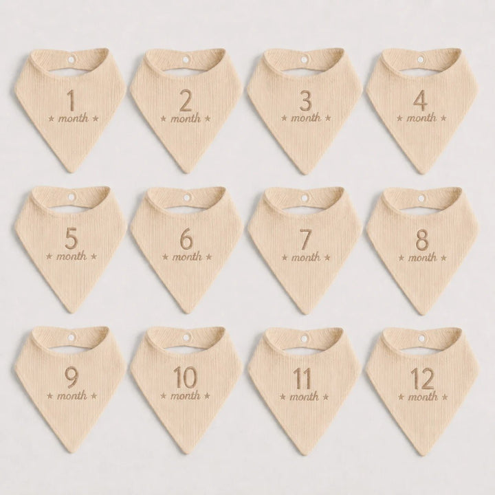 Set of 12 beige baby bandannas with month numbers on a light gray background