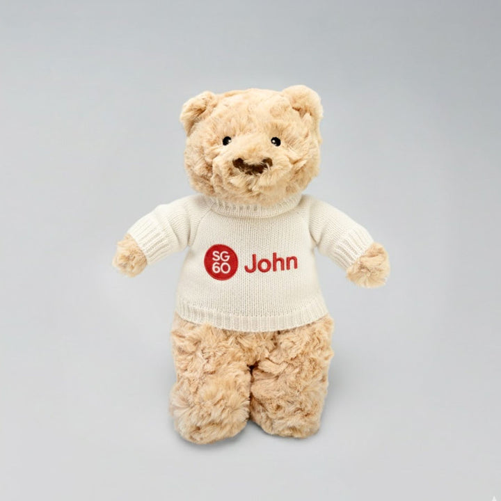 Teddy bear wearing a sweater with 'SG 60 John' on a gray background