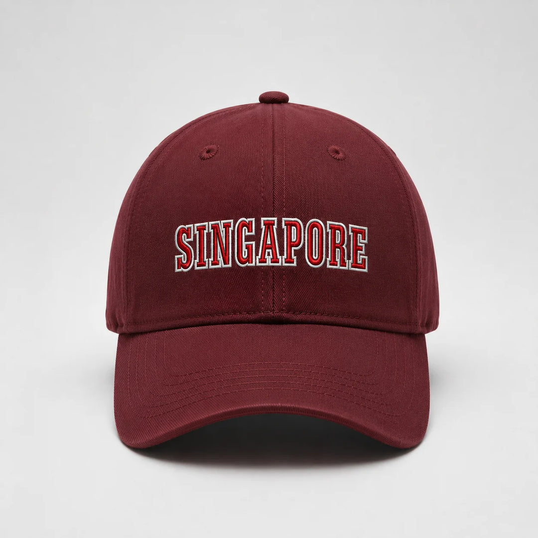 A maroon baseball cap featuring 'SINGAPORE' embroidered in arched red letters with a white outline on the front, set against a plain light gray background.